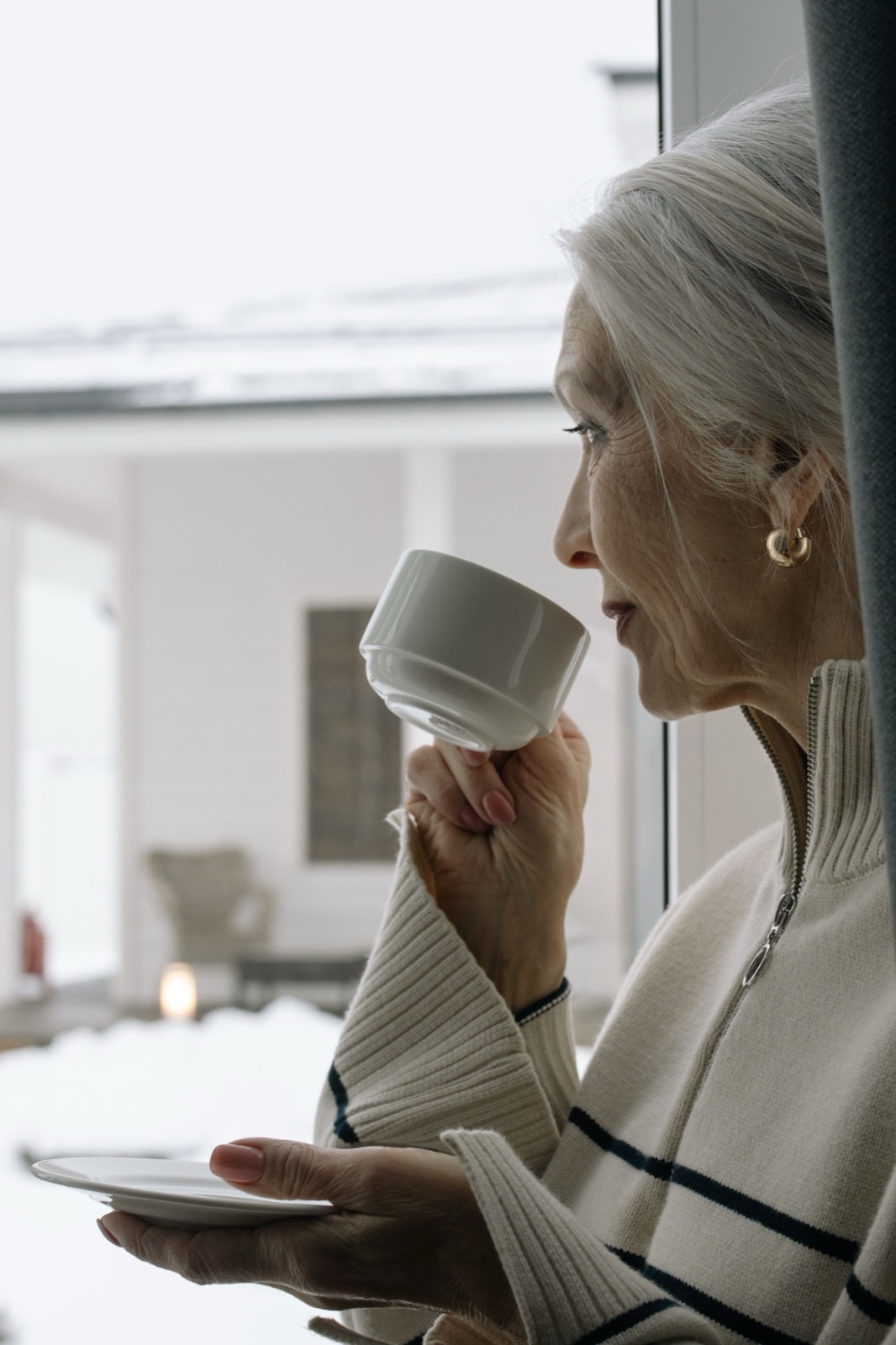 A woman holding a cup of tea by the window, deep in thought