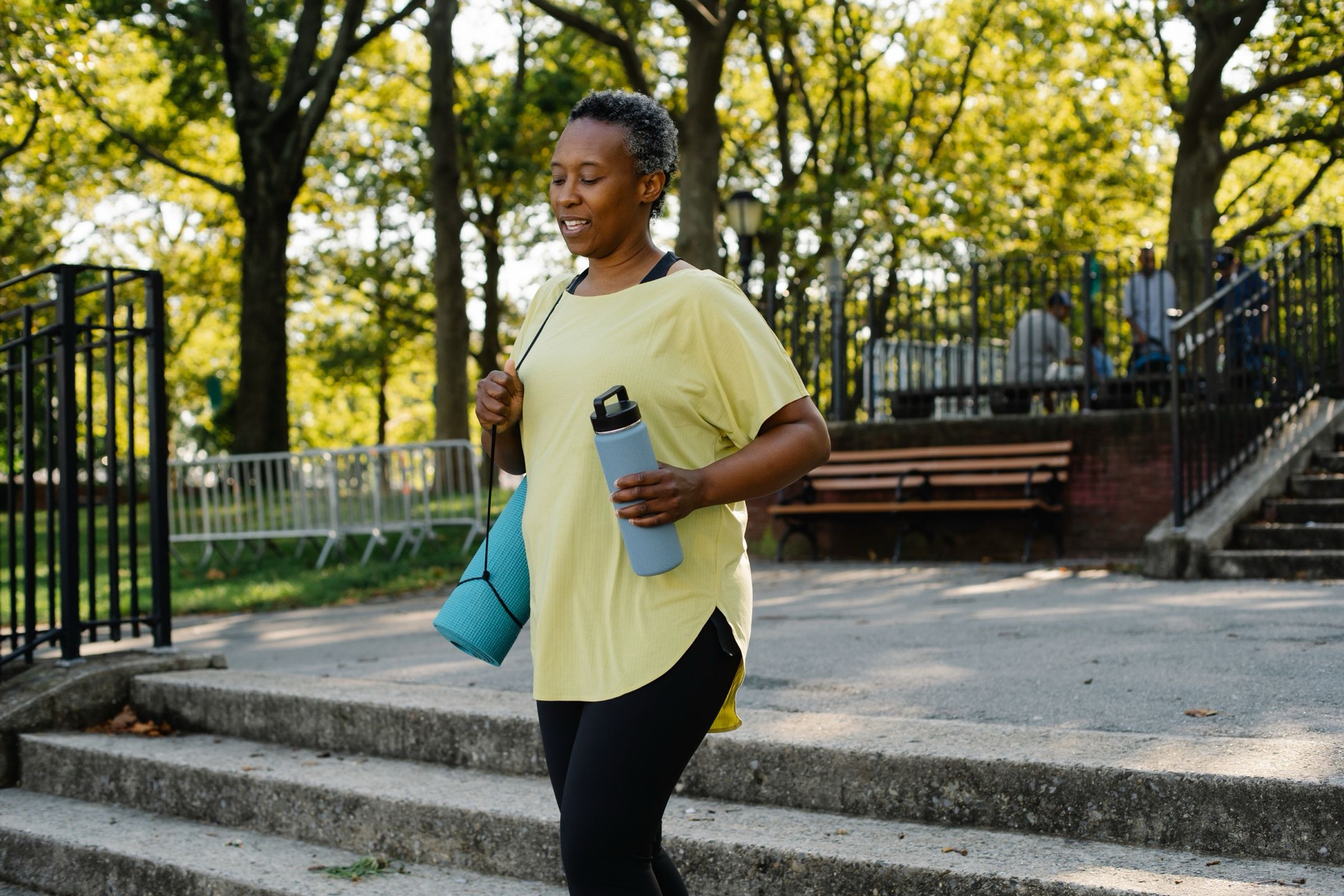 A woman out for a walk in the park with a water bottle and yoga mat